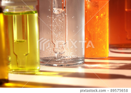 Different cosmetic glass bottles standing in a row on light background. Macro. Soft focus. Abstract colorful pattern in the sunlight. Red, green and yellow shades. Front view with copy space Different cosmetic glass bottles standing in a row on light background. Macro. Soft focus. Abstract colorful pattern in the sunlight. Red, green and yellow shades. Front view with copy space 89575658