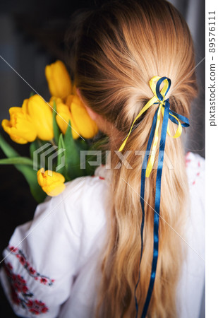 A little Ukrainian girl in traditional clothes holds a yellow tulips in her hands 89576111
