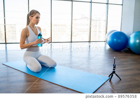 Sports coach sitting in front of a smartphone camera records video lessons. Distance fitness training concept Sports coach sitting in front of a smartphone camera records video lessons. Distance fitness training concept 89576358