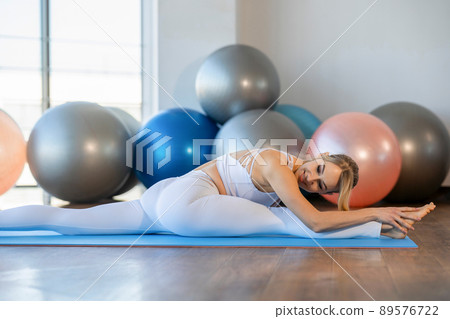 Pretty girl doing twine on yoga mat. .Flexible girl stretching indoors Pretty girl doing twine on yoga mat. .Flexible girl stretching indoors 89576722
