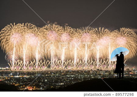 A silhouette of a couple hiding behind an umbrella and kissing at a fireworks display. 89577298