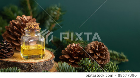 Glass bottle with conifer essential oil near fir branches and pine cones on green close up 89577390