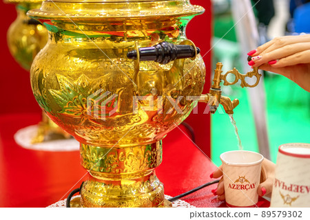 Azerbaijani tea Azercay. Girl pours hot water from samovar into paper cup with traditional Azerbaijani tea. Azerbaijani tea Azercay. Girl pours hot water from samovar into paper cup with traditional Azerbaijani tea. 89579302
