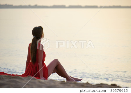 Young happy woman in red dress relaxing on sandy beach by seaside enjoying warm tropical morning. Young happy woman in red dress relaxing on sandy beach by seaside enjoying warm tropical morning. 89579615