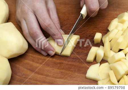 Woman's hand with a knife cutting slicing potatoes on wooden board in kitchen. Healthy eating and lifestyle. View from above close-up 89579708