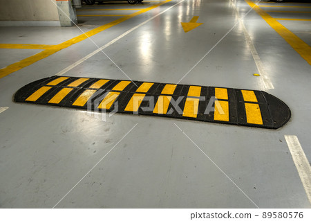 Striped black and yellow speed bump on a road. Striped black and yellow speed bump on a road. 89580576