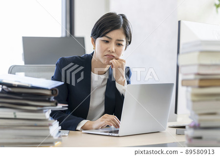 辦公桌工作一位年輕的女商人，一邊看著筆記本電腦的屏幕一邊思考 89580913