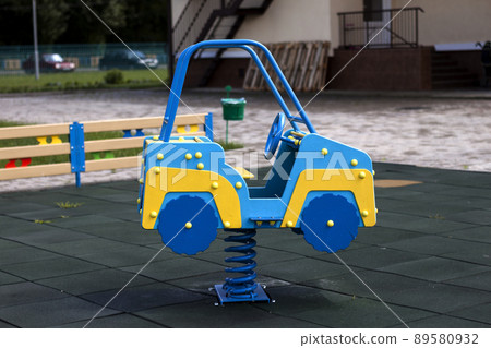 New modern plastic bright colorful blue and yellow big toy car on spring on nursery playground with soft rubber flooring on bright sunny summer day. Perfect place for children activities outdoors. New modern plastic bright colorful blue and yellow big toy car on spring on nursery playground with soft rubber flooring on bright sunny summer day. Perfect place for children activities outdoors. 89580932
