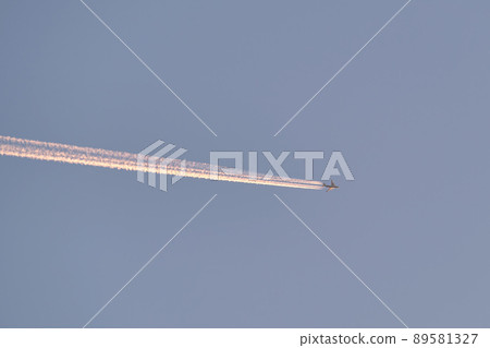 Distant passenger jet plane flying on high altitude on clear blue sky leaving white smoke trace of contrail behind. Air transportation concept 89581327