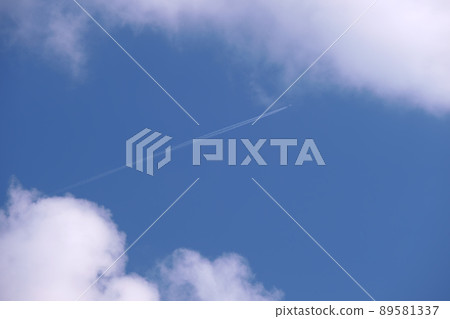 Distant passenger jet plane flying on high altitude on blue sky with white clouds leaving smoke trace of contrail behind. Air traveling concept. 89581337