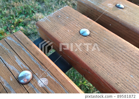 Close-up of wooden boards fastened with metal nails on a bench outdoors. 89581872