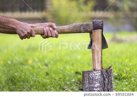 Close-up of strong muscular man hands cutting with old sharp iron ax through chunk of firewood. Close-up of strong muscular man hands cutting with old sharp iron ax through chunk of firewood. 89581884