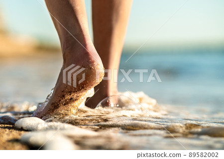 Close up of woman feet walking barefoot on sand beach in sea water. Vacation, travel and freedom concept. People relaxing in summer. 89582002