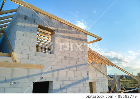 Aerial view of unfinished frame of private house with aerated lightweight concrete walls and wooden roof frame under construction. Aerial view of unfinished frame of private house with aerated lightweight concrete walls and wooden roof frame under construction. 89582779