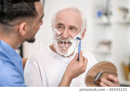 Pensioner gazing at a volunteer shaving off his stubble Pensioner gazing at a volunteer shaving off his stubble 89583220