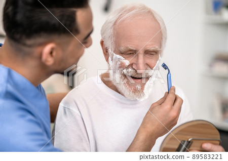 Caring volunteer giving a pleased old man a shave 89583221