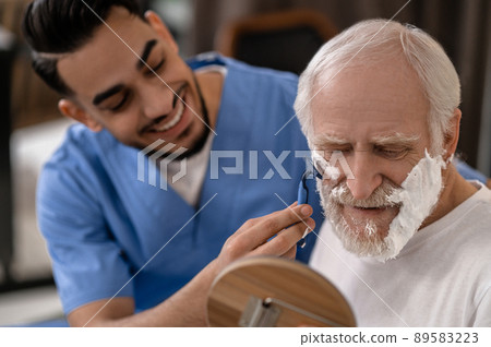 Cheerful volunteer giving an elderly person a shave 89583223