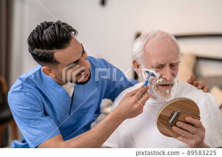 Joyous young man shaving a serious old gentleman Joyous young man shaving a serious old gentleman 89583225