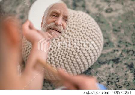 Discontented elderly man examining his reflection in the looking glass Discontented elderly man examining his reflection in the looking glass 89583231