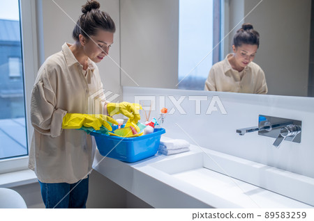 A young woman with a box with detergents in the bathroom 89583259