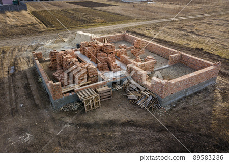 Aerial view of building site. Trenches dug in ground and filled with cement as foundation for future house, brick basement floor and stacks of brick for construction. Aerial view of building site. Trenches dug in ground and filled with cement as foundation for future house, brick basement floor and stacks of brick for construction. 89583286