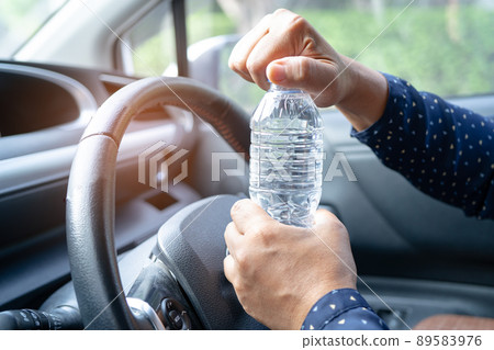 Asian woman driver holding bottle for drink water while driving a car. Plastic hot water bottle cause fire. Asian woman driver holding bottle for drink water while driving a car. Plastic hot water bottle cause fire. 89583976
