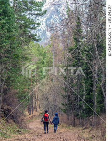 Mom and son are going hiking on a forest road uphill. Mom and son are going hiking on a forest road uphill. 89584207