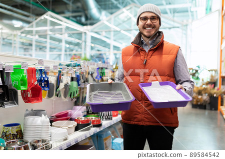 a young man chooses a cat litter box in a pet store for his pet a young man chooses a cat litter box in a pet store for his pet 89584542
