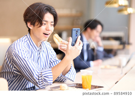 一個年輕人在咖啡館邊看智能手機邊吃飯 89584910