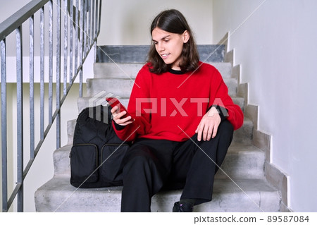 Young male sitting on stairs using smartphone Young male sitting on stairs using smartphone 89587084
