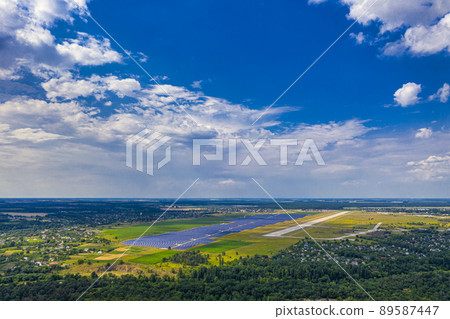 Top view of the power plant with solar panels and the aerodrome. Beautiful green fields, blue sky, clouds. 89587447