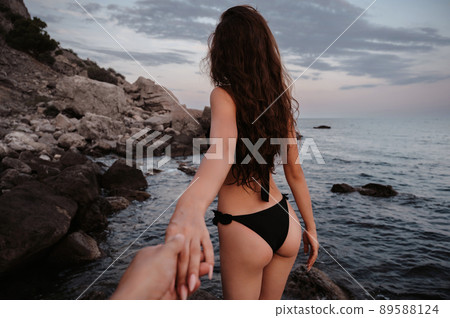 Follow me. A beautiful girl with sexy figure in a swimsuit holds her boyfriend's hand on beach by sea 89588124