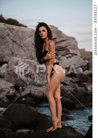 girl in a black swimsuit stands sexy on rocks on beach by the sea in summer girl in a black swimsuit stands sexy on rocks on beach by the sea in summer 89588127
