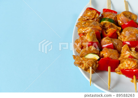 raw marinated meat on wooden skewers, pork, chicken, beef in white plate on light blue background. raw marinated meat on wooden skewers, pork, chicken, beef in white plate on light blue background. 89588263
