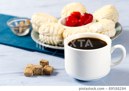 White Cup of americano coffee, and white marshmallow or Zephyr , on a light blue wooden background. White Cup of americano coffee, and white marshmallow or Zephyr , on a light blue wooden background. 89588284