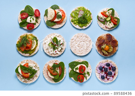 set of rice cakes on light blue background. healfy food rice cake sandwich isolated on light blue background. Rice cakes with Basil, tomatoes, avacado, cheese and red trout or salmon fish, mozerella 89588436