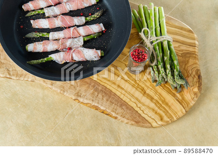 Tasty bacon around asparagus in frying pan. Fresh asparagus on wood board ready for cooking. healthy eating recipes concept 89588470