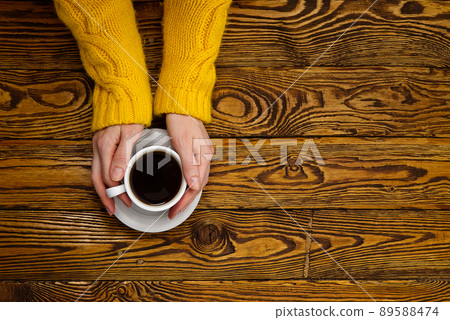 coffee mug in hand on old wooden table top view with copy space. woman in cozy yellow home sweater holding a mug of coffee while enjoying a drink coffee mug in hand on old wooden table top view with copy space. woman in cozy yellow home sweater holding a mug of coffee while enjoying a drink 89588474