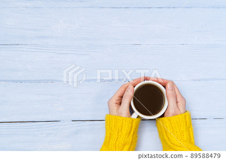 coffee mug in hand on old wooden table top view with copy space. woman in cozy yellow home sweater holding a mug of coffee while enjoying a drink coffee mug in hand on old wooden table top view with copy space. woman in cozy yellow home sweater holding a mug of coffee while enjoying a drink 89588479