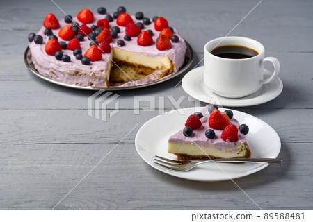 Piece of home made Cheesecake with berries on plate and mug of Americano coffee. Cheesecake with Strawberry, blueberry and raspberry on grey wooden background. Piece of home made Cheesecake with berries on plate and mug of Americano coffee. Cheesecake with Strawberry, blueberry and raspberry on grey wooden background. 89588481