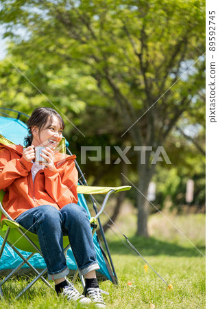 A smiling young woman enjoying a solo camp with a drink on a sunny day 89592745