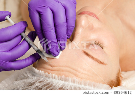 A cosmetologist performs a procedure of rejuvenating injections for the face to tighten and smooth out wrinkles on the skin of a woman's face. Cosmetic skin care in a beauty salon. 89594612
