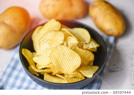 Crispy potato chips on the kitchen table and fresh raw potatoes on wooden background, Potato chips snack on bowl 89597444