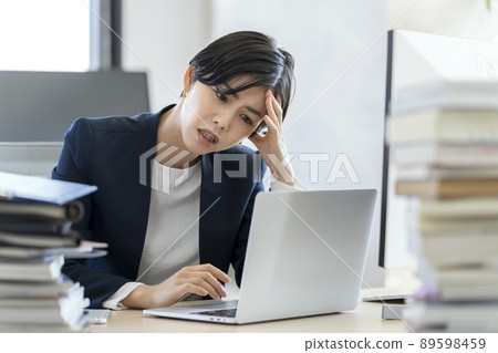 Desk work A business woman holding her head while looking at the screen of a laptop computer 89598459
