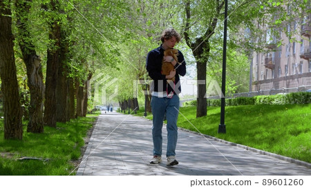 A young man walks with his Pomeranian dog in the park in the morning. The dog is tired and refuses to go. A walk in the fresh air. A young man walks with his Pomeranian dog in the park in the morning. The dog is tired and refuses to go. A walk in the fresh air. 89601260