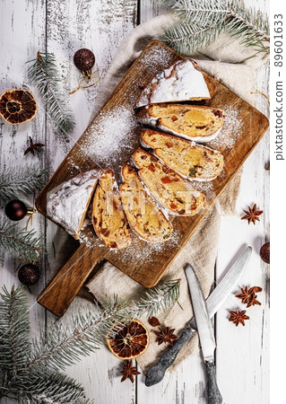 Christmas stollen on a cutting board. Wooden white table background. Traditional Christmas pastry with marzipan, nuts, raisins and dried fruit. Top view Christmas stollen on a cutting board. Wooden white table background. Traditional Christmas pastry with marzipan, nuts, raisins and dried fruit. Top view 89601633