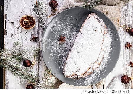 Christmas stollen on a gray plate. Wooden white table background. Traditional Christmas pastry with marzipan, nuts and raisins. Top view Christmas stollen on a gray plate. Wooden white table background. Traditional Christmas pastry with marzipan, nuts and raisins. Top view 89601636