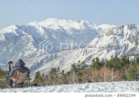 A man sitting in a camping chair overlooking the mountains of the Northern Alps from the Nishihotakadake ridgeline in early spring 89602294