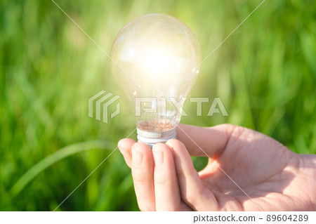 Hand holding a lamp on a background of green grass. Concept of green electricity, startup, creative eco idea. A place to meditate or reboot. Hand holding a lamp on a background of green grass. Concept of green electricity, startup, creative eco idea. A place to meditate or reboot. 89604289