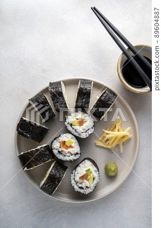 Sushi on round plate with chopsticks, soy sauce. ginger. Homemade rolls with salmon, avocado and cucumber. 89604887